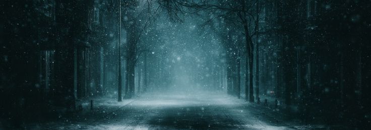 An empty snow-covered street with one distant light